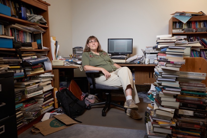 Dr. Elizabeth Anderson seated at a desk surrounded by stacks of books