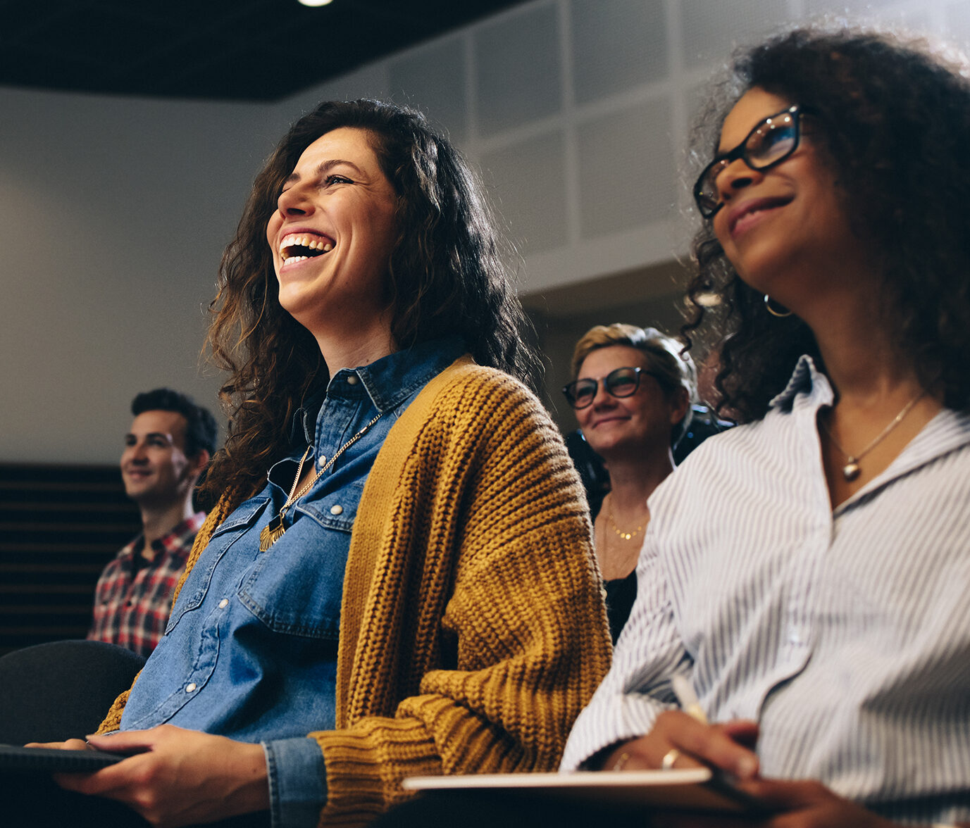 two smiling women seated in a crowd at a conference