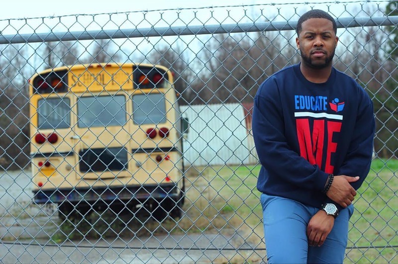 Man standing against a fence with a school bus in the background on the left