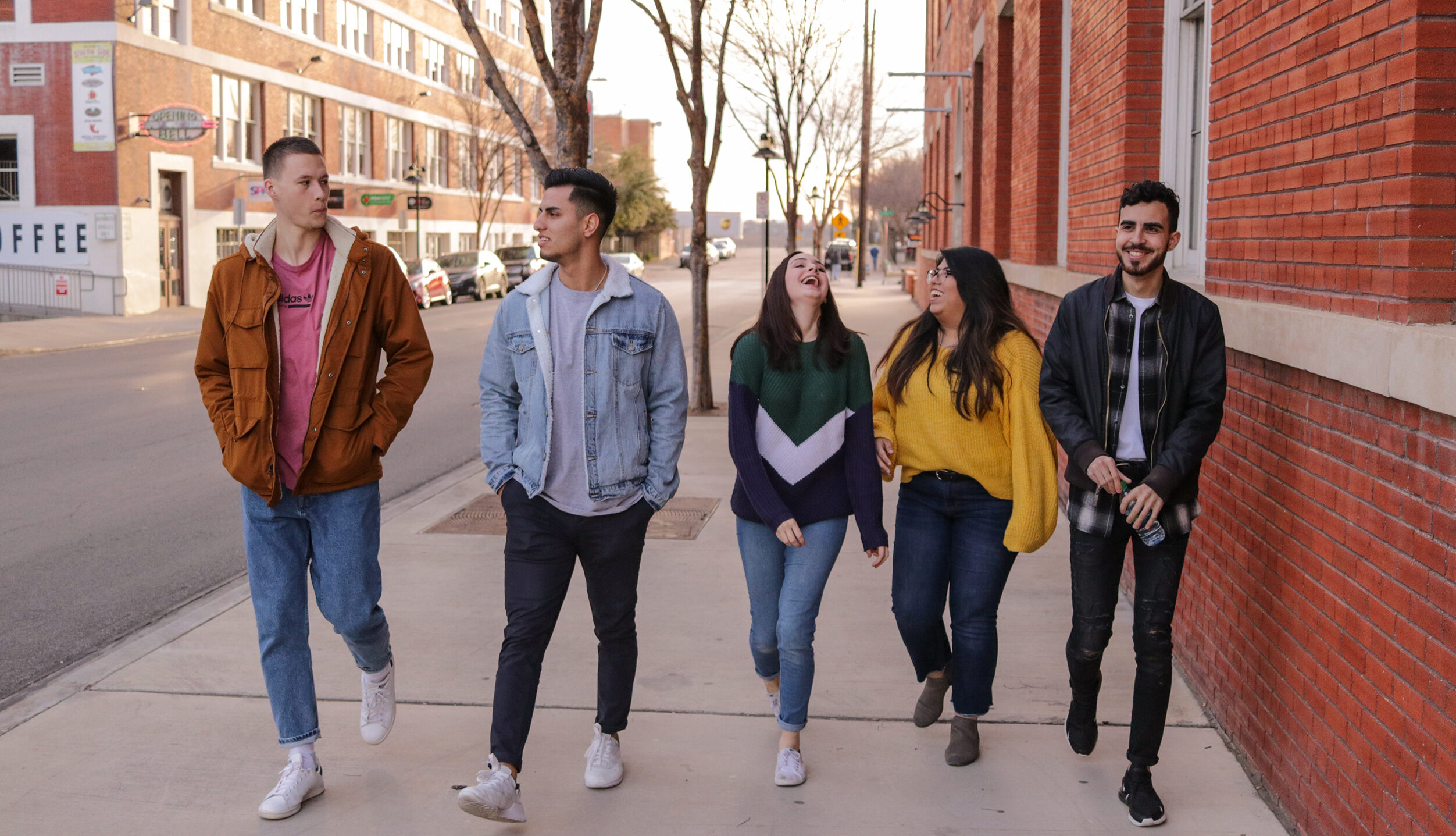 five young people walking down a sidewalk laughing and talking